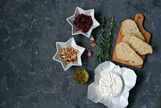 Ingredients for cooking baked camembert: camembert cheese, dried cranberries, fresh rosemary, olive oil, garlic, walnuts, white bread for toasts. Top view, copy space.