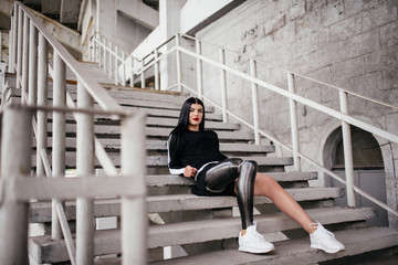 Photo of atlethic disabled woman in sportswear with prosthetic leg, sitting at the stairs outdoor...