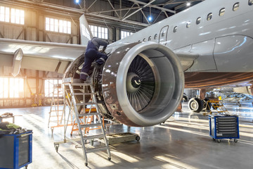 Mechanic specialist repairs the maintenance of engine of a passenger aircraft in a hangar - obrazy, fototapety, plakaty