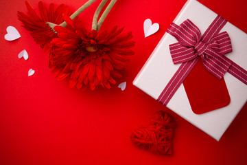 Gift, red gerberas and a heart on a red background.