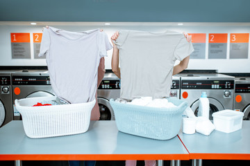 Women sorting clothes near the table with baskets in the self service laundry, closing face with t-shirts