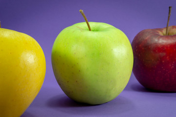 Yellow, green and red apples on purple background