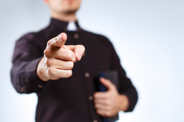 Priest pointing into the camera on grey background