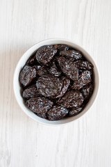 Full bowl of dry prunes on a white wooden background, top view. Overhead, flat lay, from above.