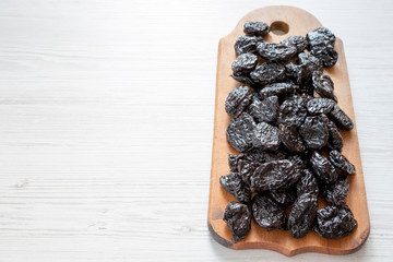 Dry prunes on rustic wooden board on a white wooden surface, side view. Copy space.