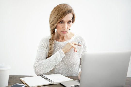 People, aging, technology and emotion concept. Amazed shocked attractive Caucasian female freelancer in her sixties staring at computer screen, being surprised with amount of work she has to do
