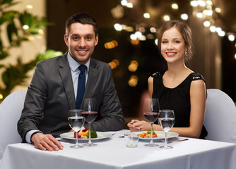 people and leisure concept - smiling couple with food and non-alcoholic red wine at restaurant over festive lights on background