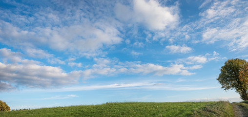 Grüne Hügelkuppe und blauer Himmel mit Wolken