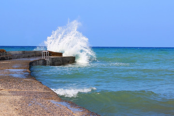 Sea water storm waves hitting the stone pier, sunny and windy day