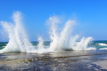 Sea water storm waves hitting the big stone on the beach on a sunny and windy day
