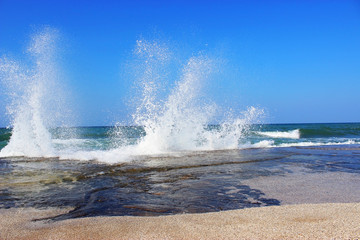 Sea water storm waves hitting the big stone on the beach on a sunny and windy day