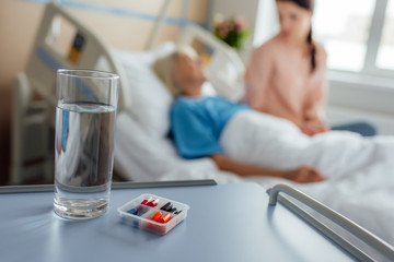 selective focus of water glass and medicine with patient and visitor on background