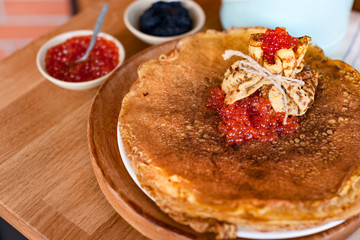 Pancakes for the traditional Russian spring holiday. Thin pancakes with red and black caviar. Wooden background and festive food.