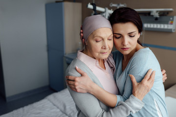 upset daughter embracing sick senior mother with cancer in hospital