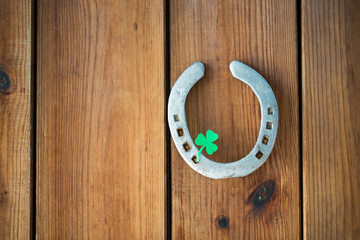 fortune, luck and st patricks day concept - horseshoe with shamrock on wooden background