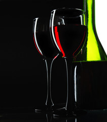 Two glasses of red wine and a green bottle. On a black background.