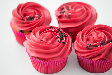 food, baking and pastry concept - close up of cupcakes or muffins with red buttercream frosting and sprinkles