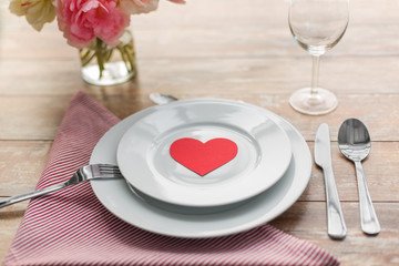 Fototapeta na wymiar valentines day, table setting and romantic dinner concept - close up of plates with cutlery, flowers in vase and napkin