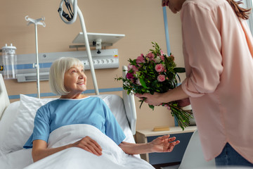 daughter presenting flowers to happy senior woman in hospital