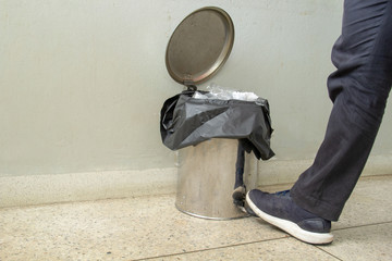 Man's foot open garbage bin on gray background and putting smartphone in it