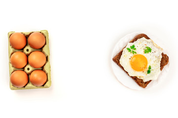 An egg cooked sunny side up on a toast and a carton of eggs, shot from above on a white background with copy space