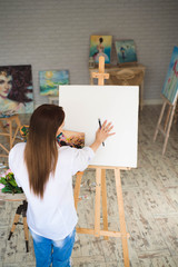 Creative pensive painter paints a colorful picture. Closeup of painting process in art workshop Creative positive woman painter paints in her studio.