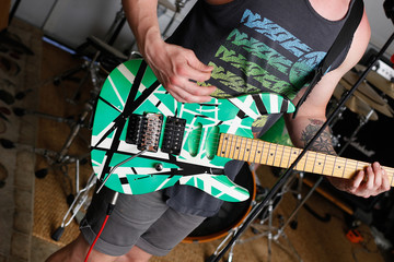 Young male guitarist playing on bright green electric guitar