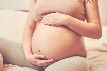 Fototapeta na wymiar Beautiful pregnant woman touching her belly and enjoying at home.