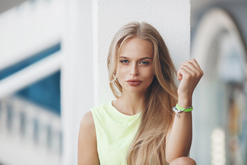 Photo of a beautiful blonde girl sitting on the railing in the hotel at sunset. Woman resting on the street.Cute blue-eyed blonde poses alone sitting on a white railing on the hotel’s outdoor terrace