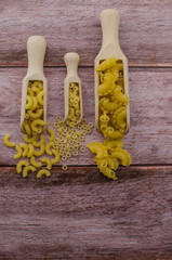 Dried pasta food selection in wooden spoons over old oak background.