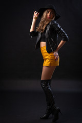 Close up studio portrait of beautiful glamour sensual woman in trendy black T-shirt, orange skirt, leather jacket and hat on black background. Healthy wavy long hairs.