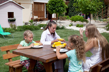 Family having dinner together on outdoor. Fresh, boiled cobs corn in dish on a wooden table