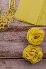 Dried pasta food selection in wooden spoons over old oak background.