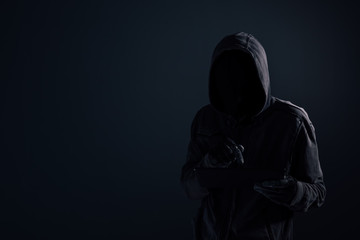 Hooded computer hacker with obscured face using digital tablet
