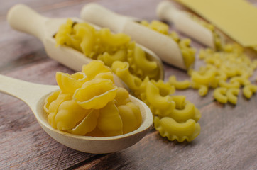 Dried pasta food selection in wooden spoons over old oak background.