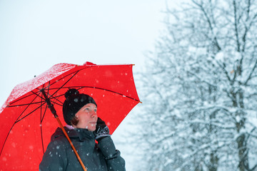 Positive woman talking on mobile phone under umbrella in snow