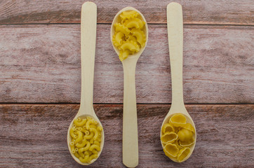 Dried pasta food selection in wooden spoons over old oak background.