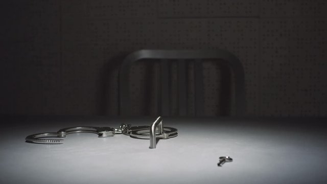Close-up parallax shot of a pair of handcuffs and a key on a table in an interrogation room.