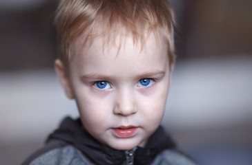 Close up portrait of cute caucasian baby boy with very serious face expression. Bright blue eyes,...
