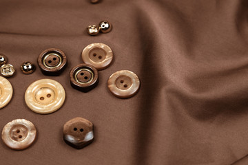 Brown fabric with a shade of chocolate is spread out on a table with folds. On fabric buttons of...