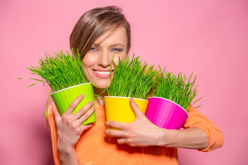 Young lady with wheatgrass in flower pots over brigh pink background