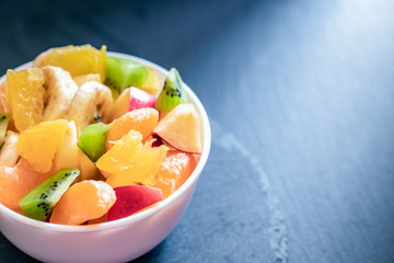 Lighted white cup with fresh fruit salad on dark grey background.
