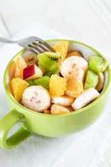 Close-up green mug with fresh fruit salad on white background.