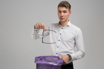 Young man throws glasses in trash isolated on white background