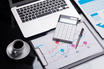 Obraz premium Modern calculator is on the notebook and on the sheet with the schedule next to the coffee Cup
