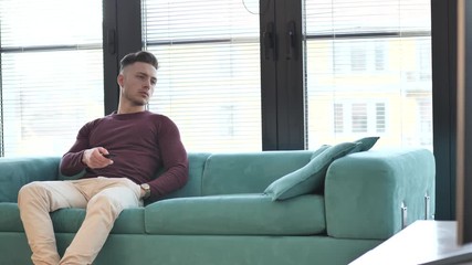 Young man sitting watching television changing the channel with the remote control