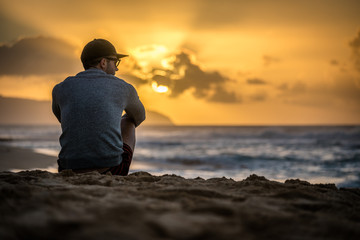 Silhouette of young caucasian male sitting on Sunset Beach in Hawaii looking out at sunset over the...