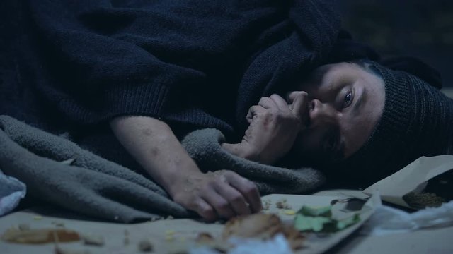 Sick hungry homeless person lying on street and eating last piece of orts