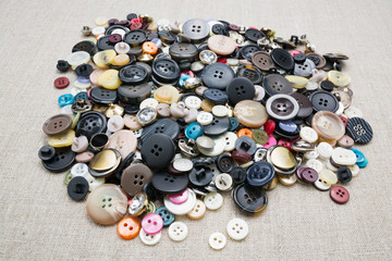 A lot of colorful sewing buttons of different colors of metal and plastic on linen light natural fabric 