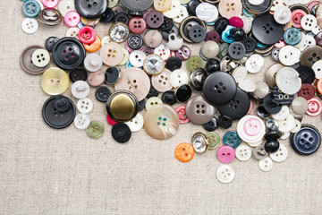A lot of colorful sewing buttons of different colors of metal and plastic on linen light natural fabric 